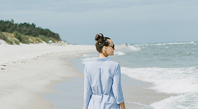 Junge Frau spaziert am Ostseestrand und blickt auf das Meer.